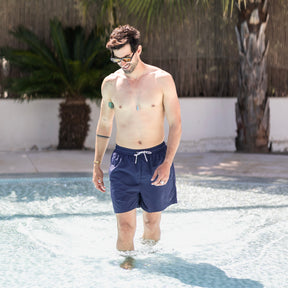 Mann trägt navyblaue Badehose 'Jay' und geht knietief im Poolwasser