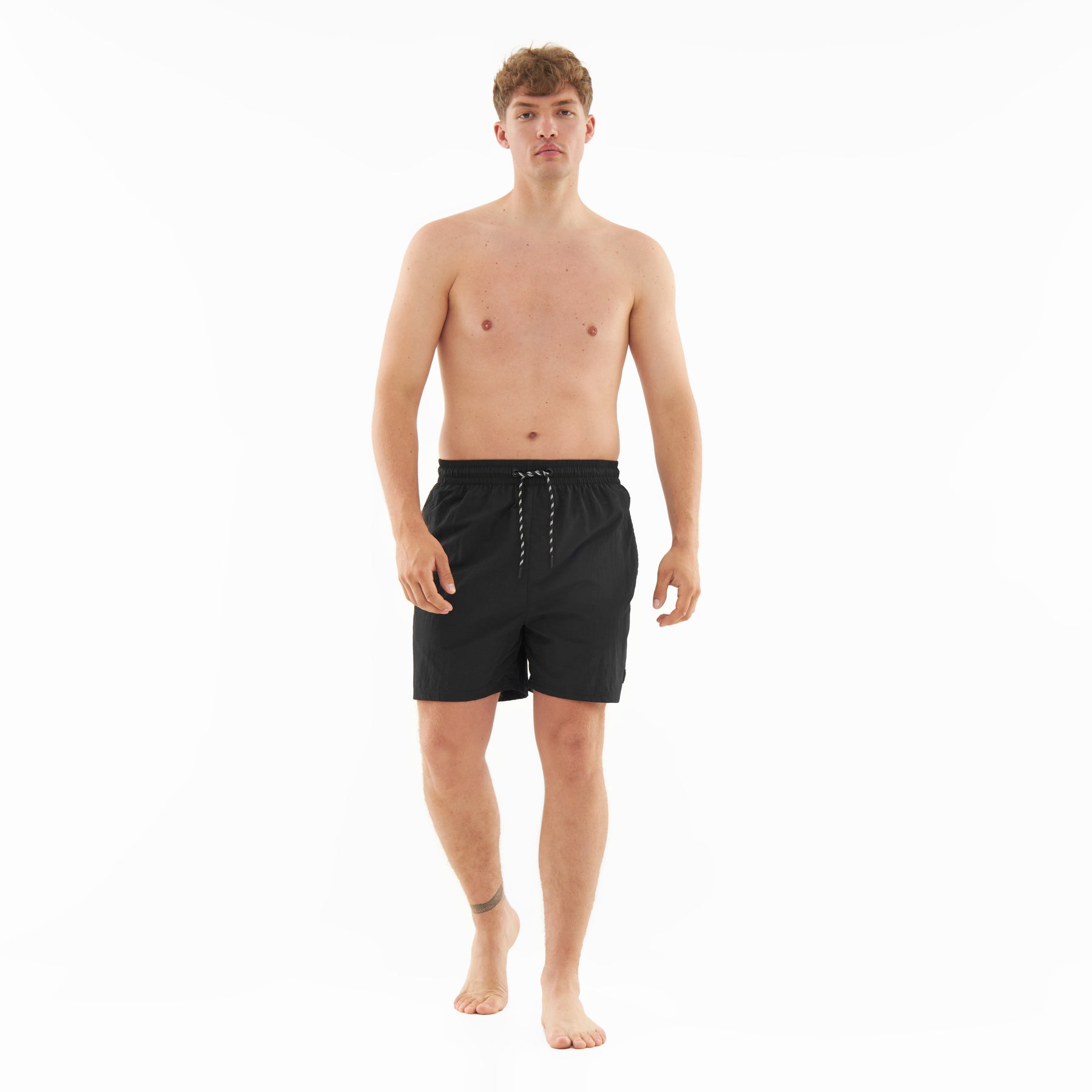 Mann trägt schwarze Badehose 'Jay' mit Kordelzug, frontal stehend, barfuß