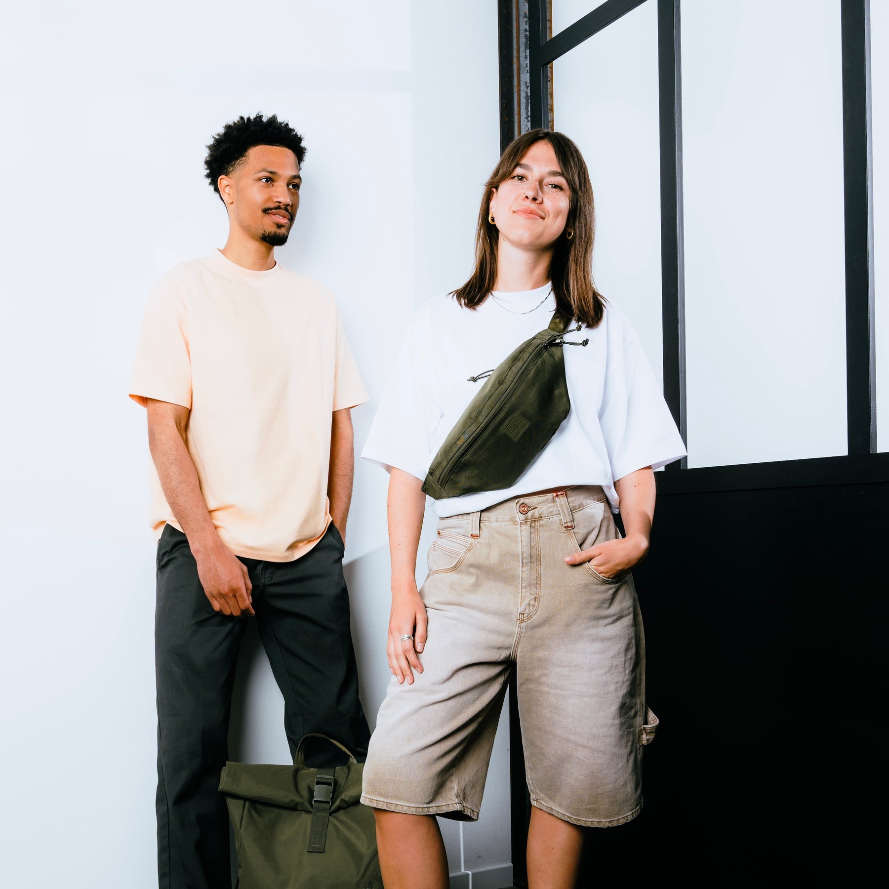 Frau trägt olivgrüne Bauchtasche 'Erik Large' von Johnny Urban quer am Oberkörper über weißem Shirt und beigen Shorts