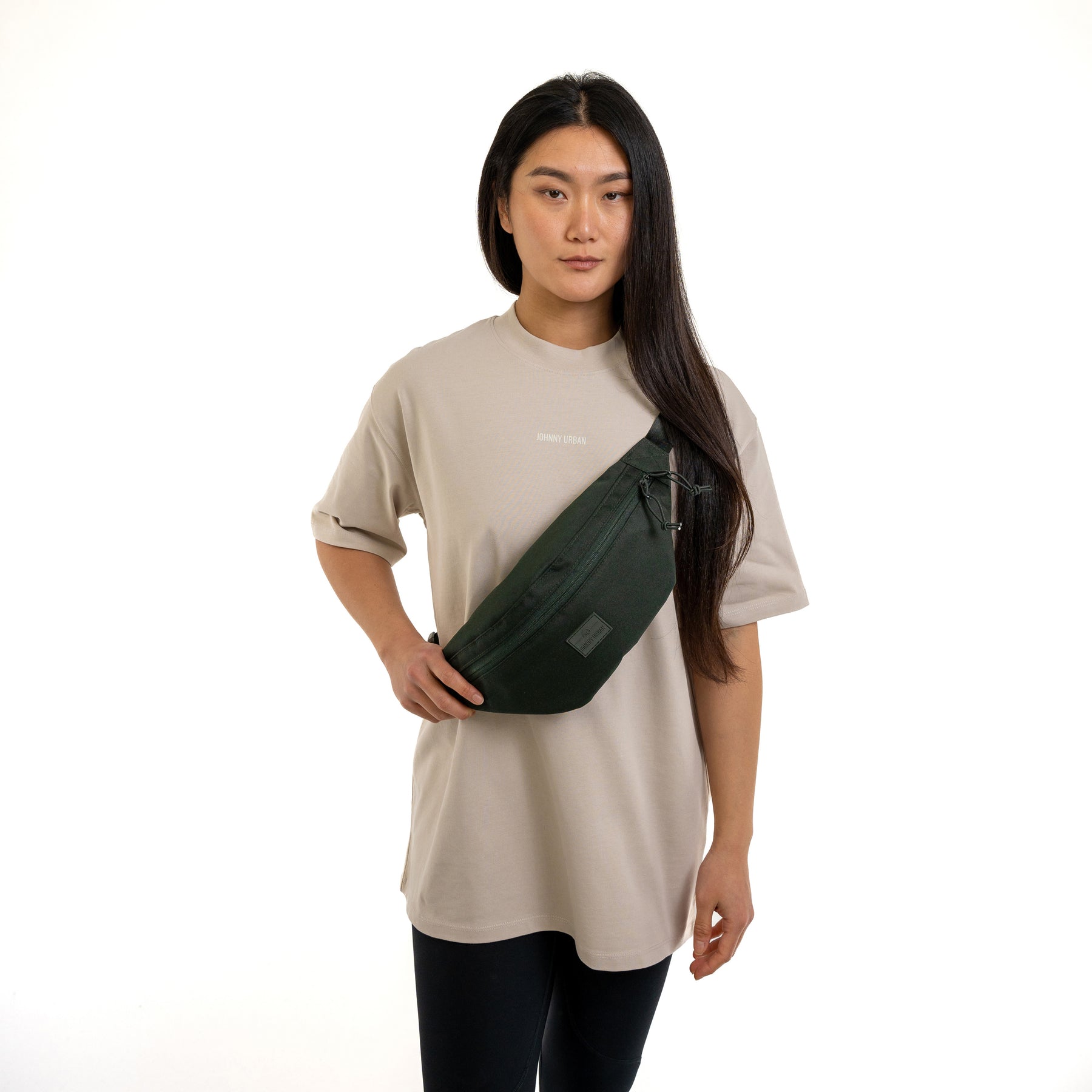 Frau trägt dunkelgrüne Johnny Urban Bauchtasche 'Erik Large' quer über die Brust, beige T-Shirt mit Logo