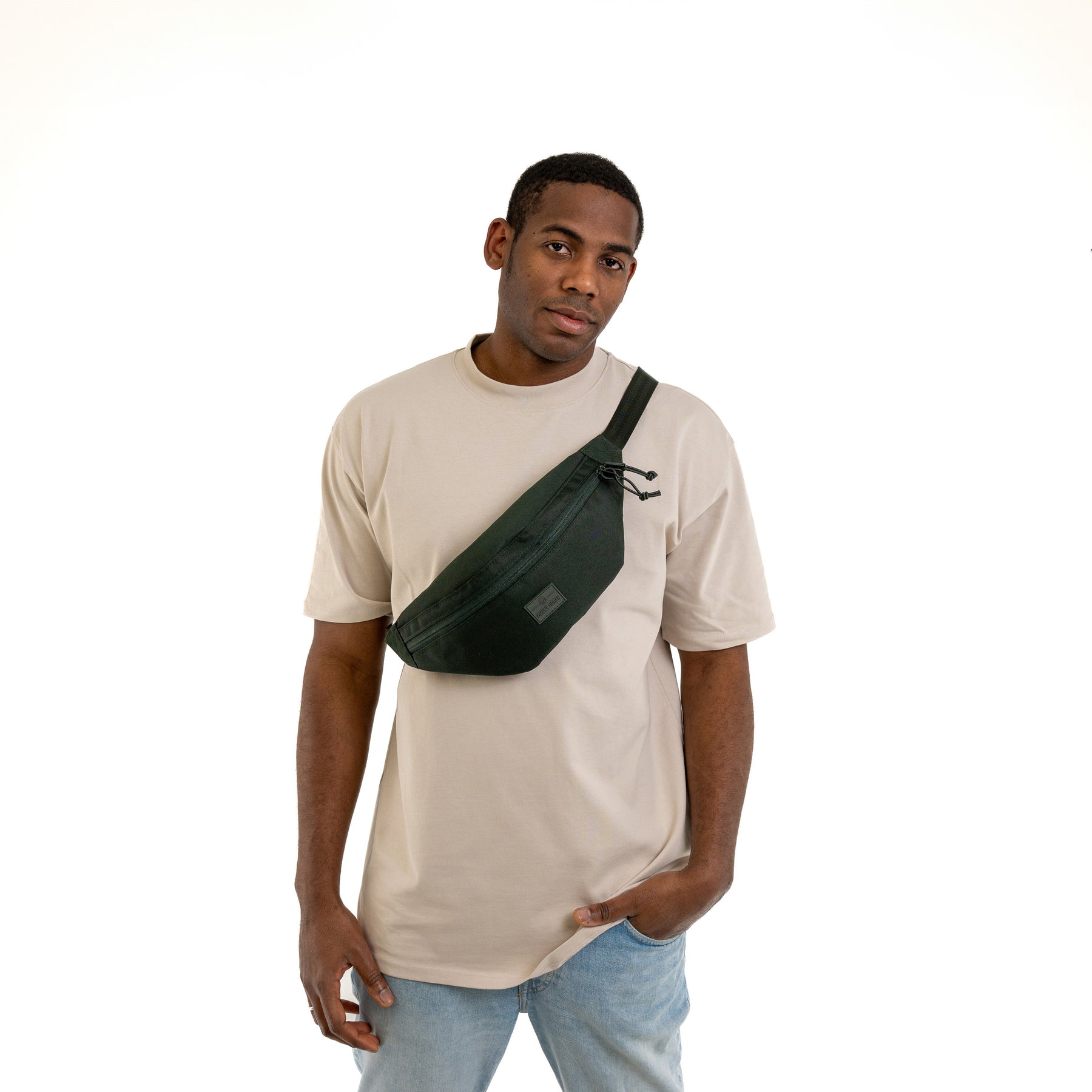 Mann trägt dunkelgrüne Johnny Urban Bauchtasche 'Erik Large' quer über die Brust mit beige T-Shirt und Jeans