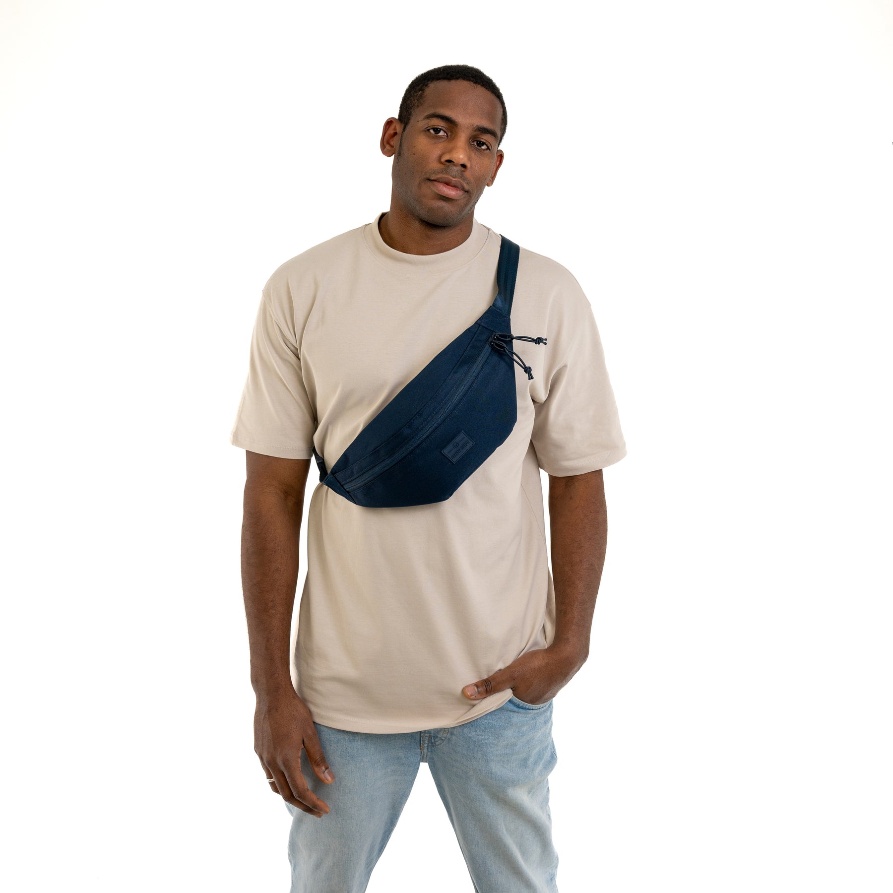 Mann trägt moderne blaue Bauchtasche 'Erik Large' von Johnny Urban quer über der Brust, beige T-Shirt, helle Jeans