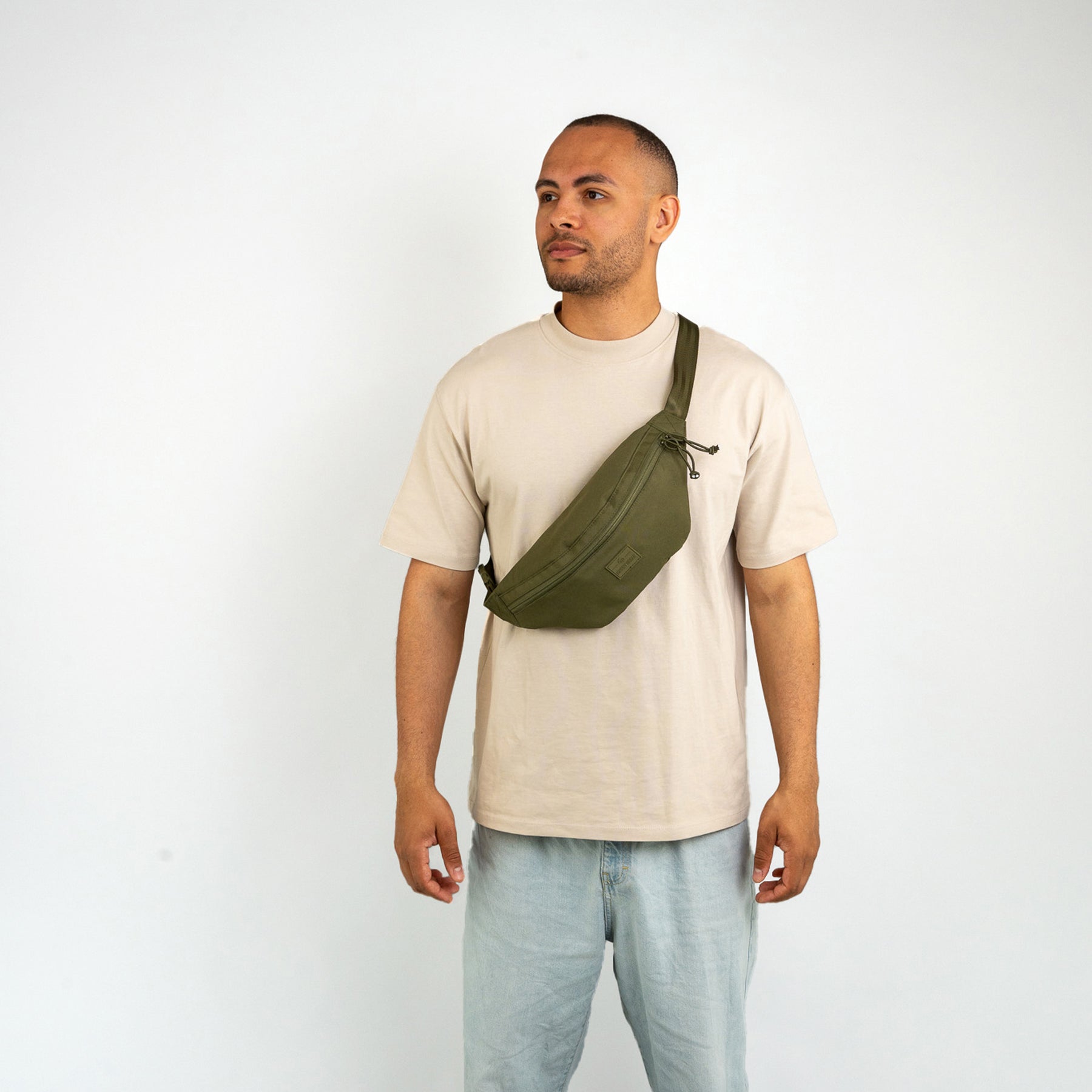 Mann trägt olivgrüne Bauchtasche ‚Erik Large‘ quer über der Brust mit hellem T-Shirt und Jeans
