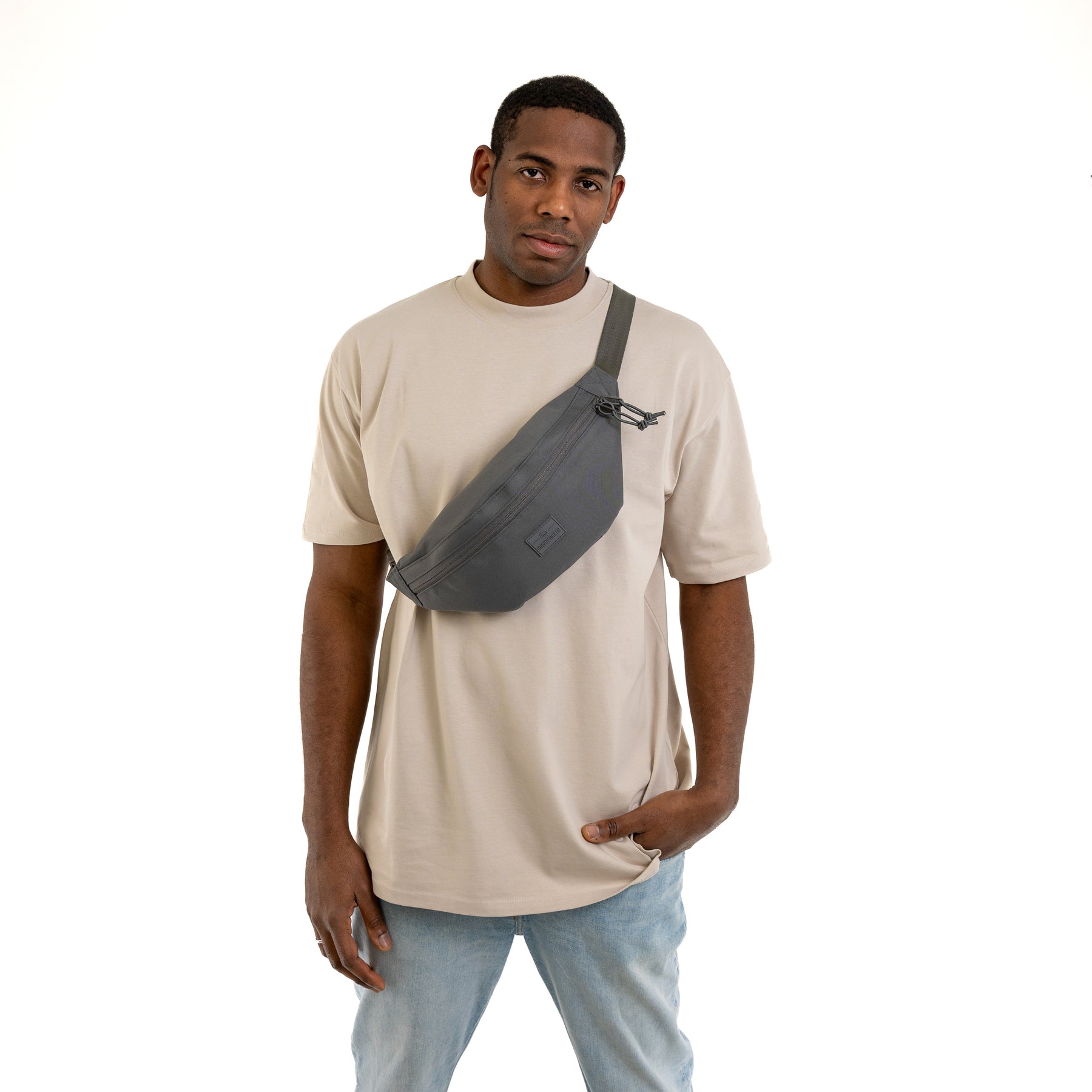 Mann trägt dunkelgraue Bauchtasche 'Erik Large' von Johnny Urban diagonal über beige T-Shirt und Jeans