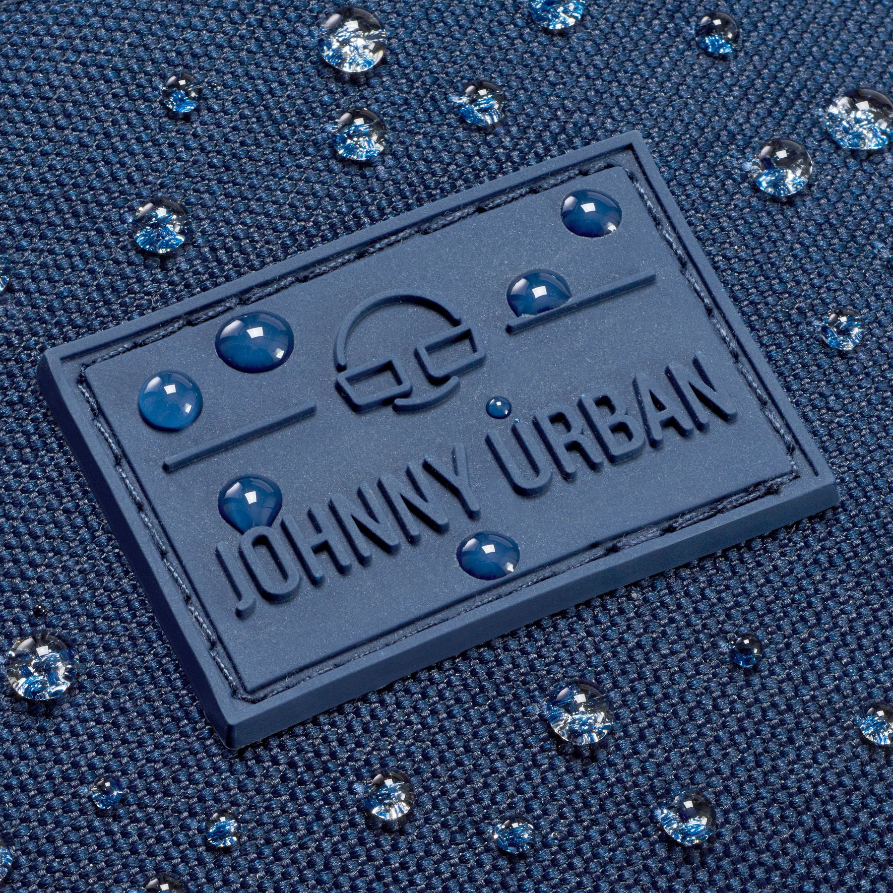 Nahaufnahme des wasserdichten blauen Gewebes mit Johnny Urban Logo und Wassertröpfchen auf der Bauchtasche Erik Large