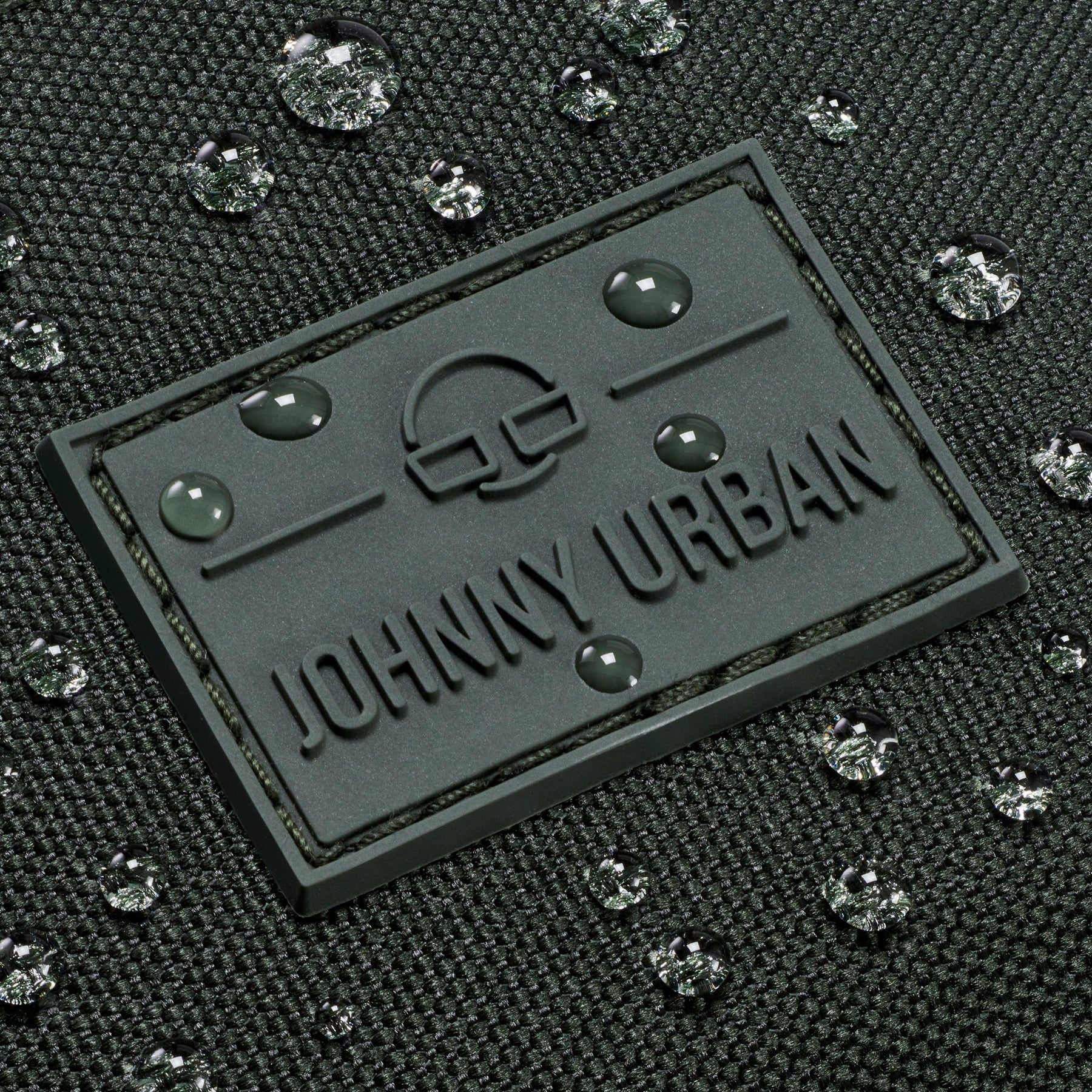 Gummilogo mit Schriftzug 'Johnny Urban' auf wasserabweisendem dunkelgrünem Stoff mit Wassertropfen