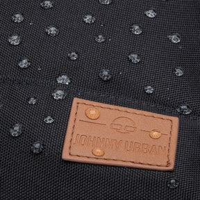 Wasserabweisendes schwarzes Material mit braunem Lederetikett 'Johnny Urban' und Wassertropfen darauf