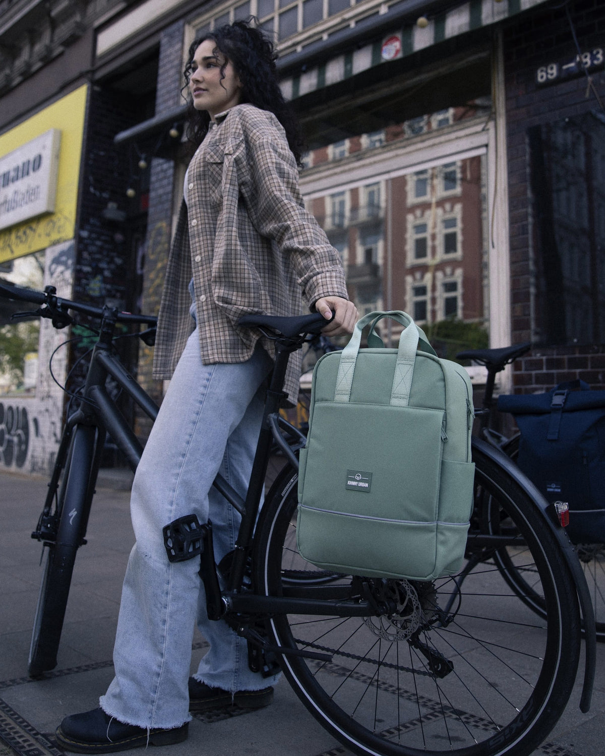 Frau lehnt an schwarzem Fahrrad mit grünen Rucksack 'Jona Medium' von Johnny Urban am Gepäckträger