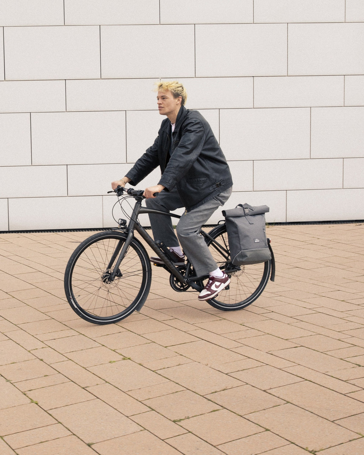 Mann fährt Fahrrad mit grauem Rolltop Rucksack 'Robin Medium' von Johnny Urban am Gepäckträger
