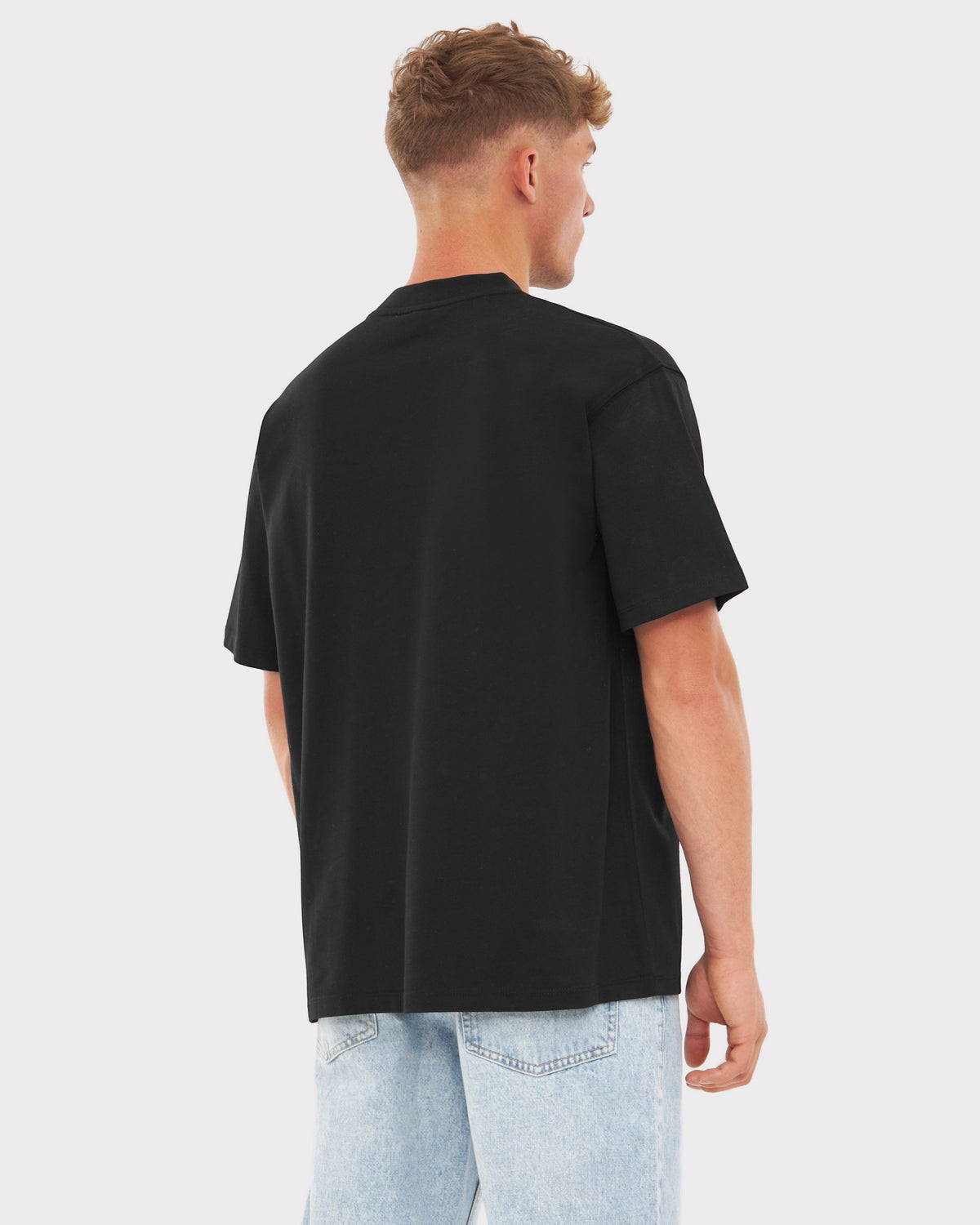 Mann trägt schwarzen Oversized-T-Shirt 'Sammy Johnny Urban' von hinten mit hellen Jeans