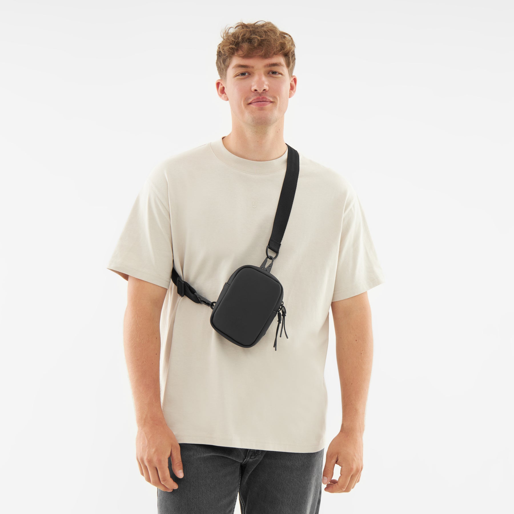 Mann trägt schwarzen Front Pack 'Toby' quer über die Brust, helles T-Shirt, dunkle Jeans