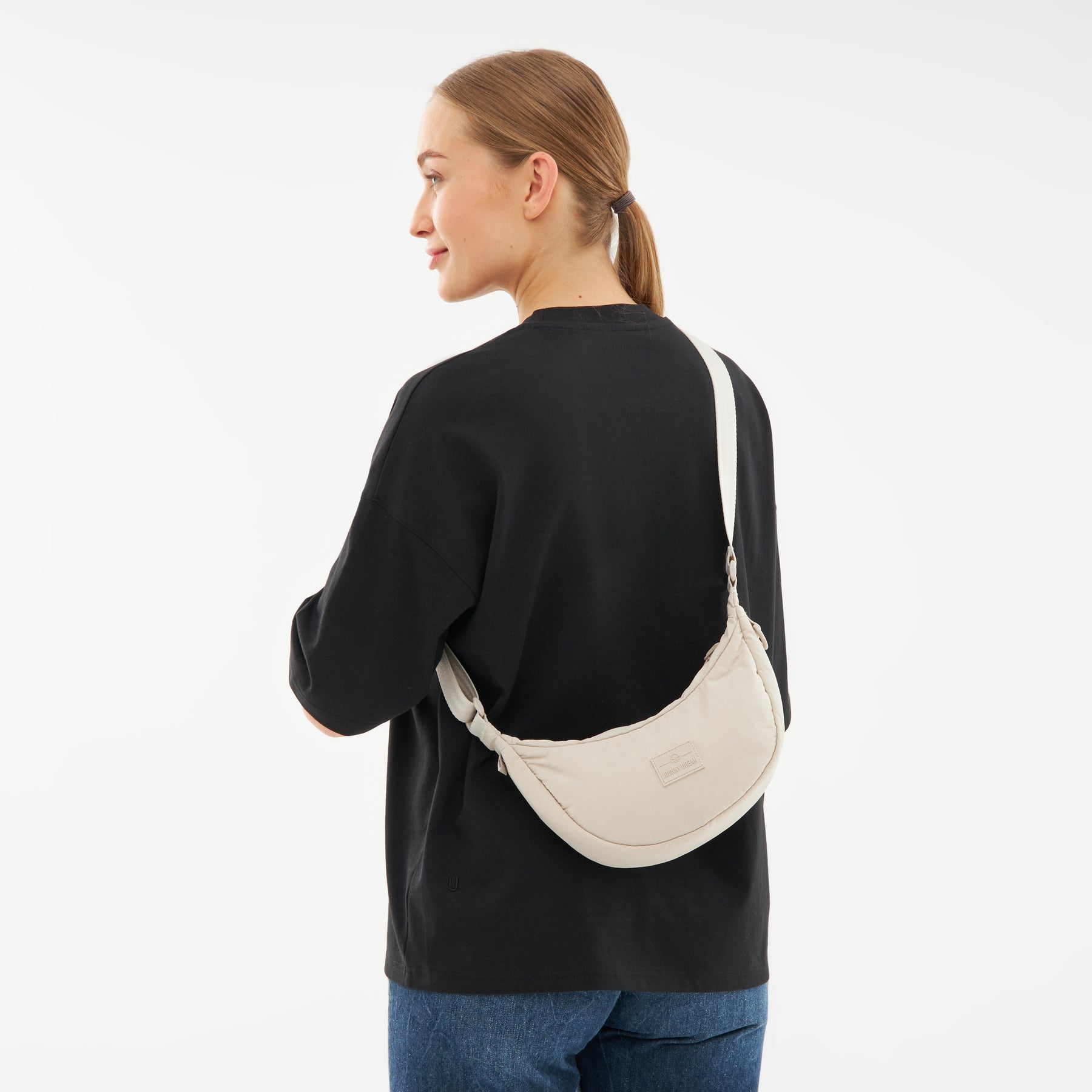 Frau von hinten mit schwarzem Sweatshirt und Jeans trägt beige Half Moon Bag 'Kaia Small' über die Schulter