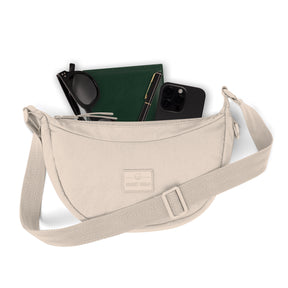 Beige kleine Half Moon Bag 'Kaia Small' von Johnny Urban mit Sonnenbrille, grünem Notizbuch, Stift und schwarzem Smartphone