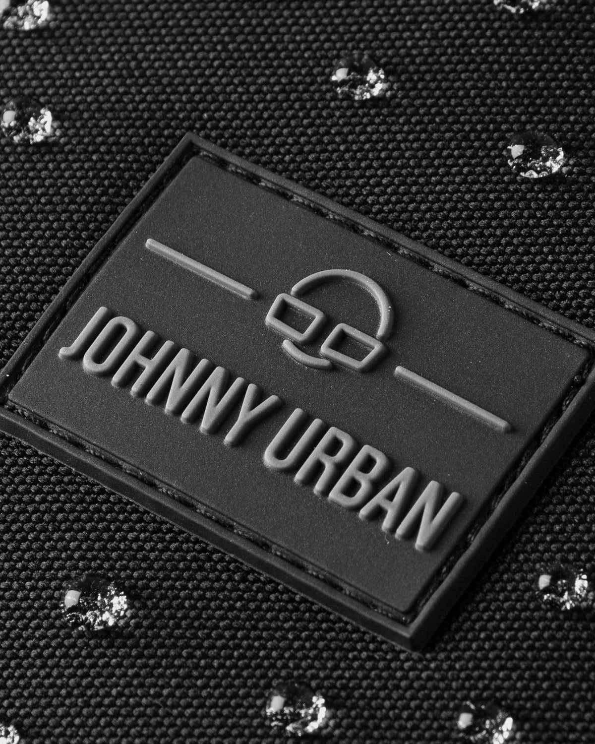 Nahe Aufnahme des schwarzen Johnny Urban Logos auf wasserabweisendem Stoff mit glänzenden Wassertropfen