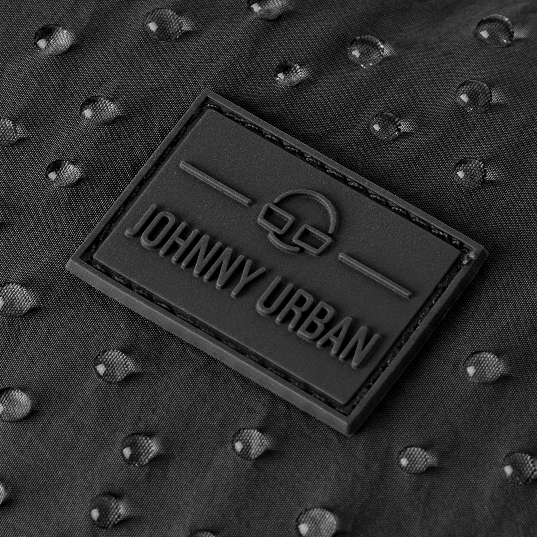 Nahaufnahme des Johnny Urban Logos auf wasserabweisendem, schwarzem Stoff mit Wassertröpfchen