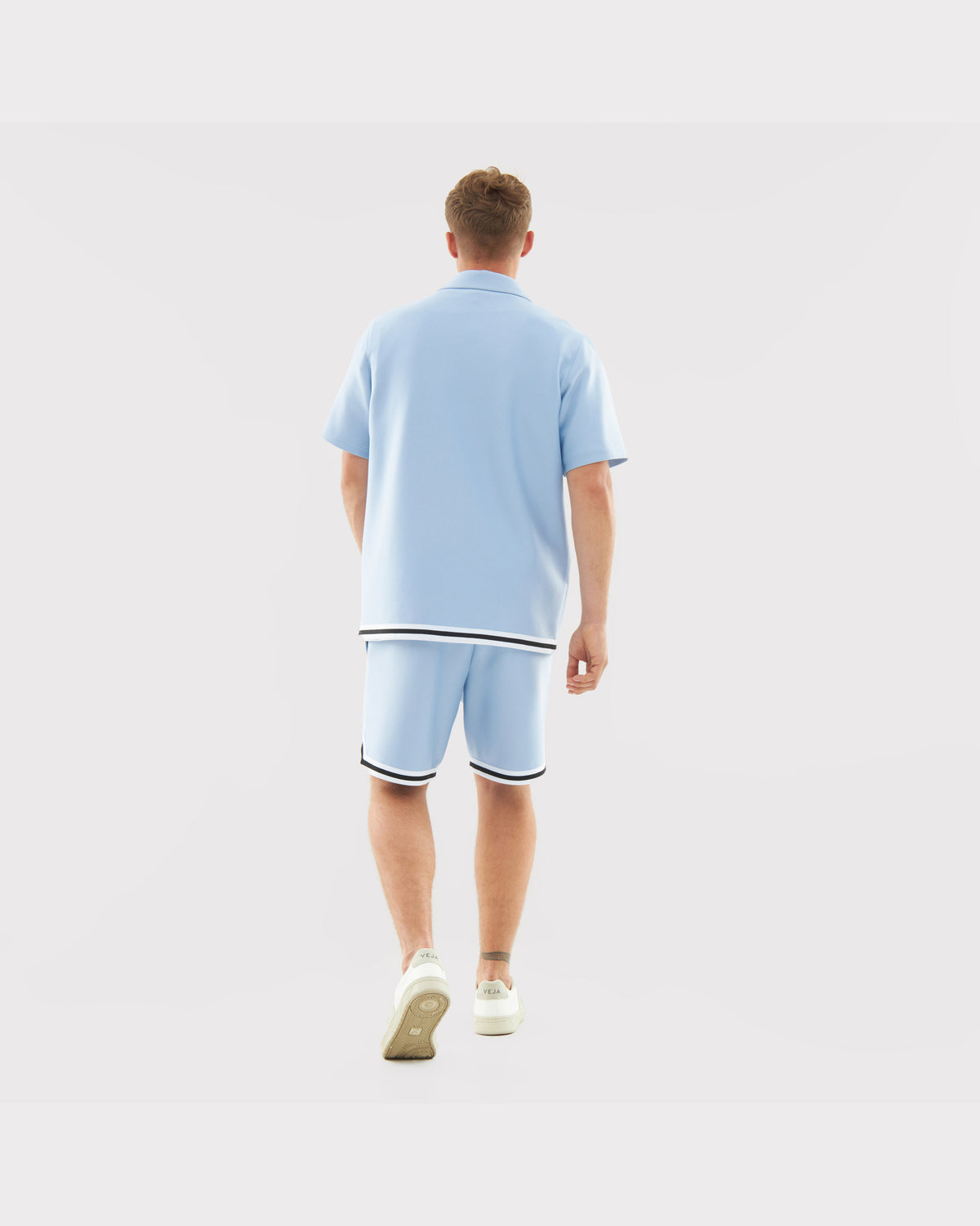 Mann von hinten trägt hellblaues, locker geschnittenes Hemd und Shorts mit schwarzen und weißen Saumstreifen