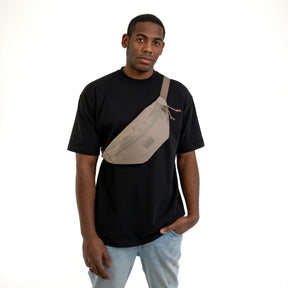 Mann trägt die große Bauchtasche ‚Erik Large‘ in desert grey über der Brust, dazu schwarzes T-Shirt und helle Jeans