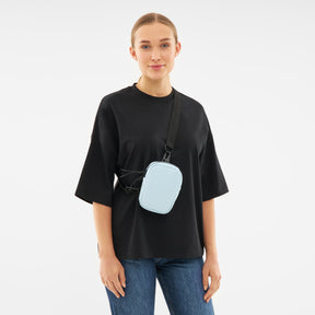 Frau trägt hellblaue Front Pack 'Toby' Crossbody-Tasche über schwarzem T-Shirt und blauen Jeans