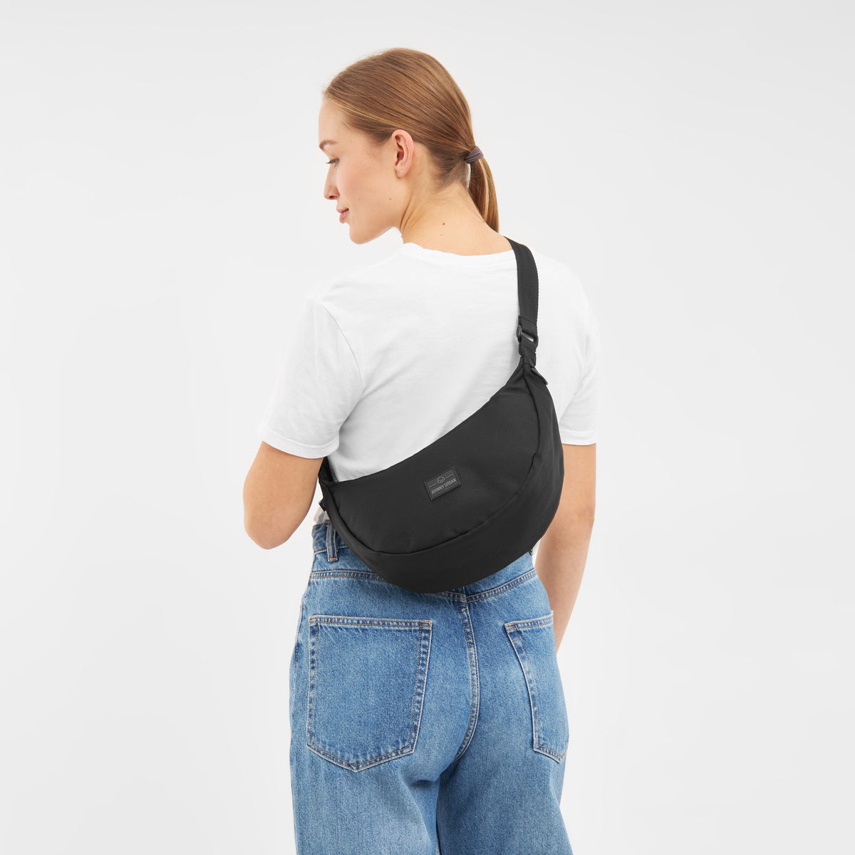 Frau von hinten mit schwarzer Half Moon Umhängetasche 'Ally Medium', weißem T-Shirt und blauen Jeans