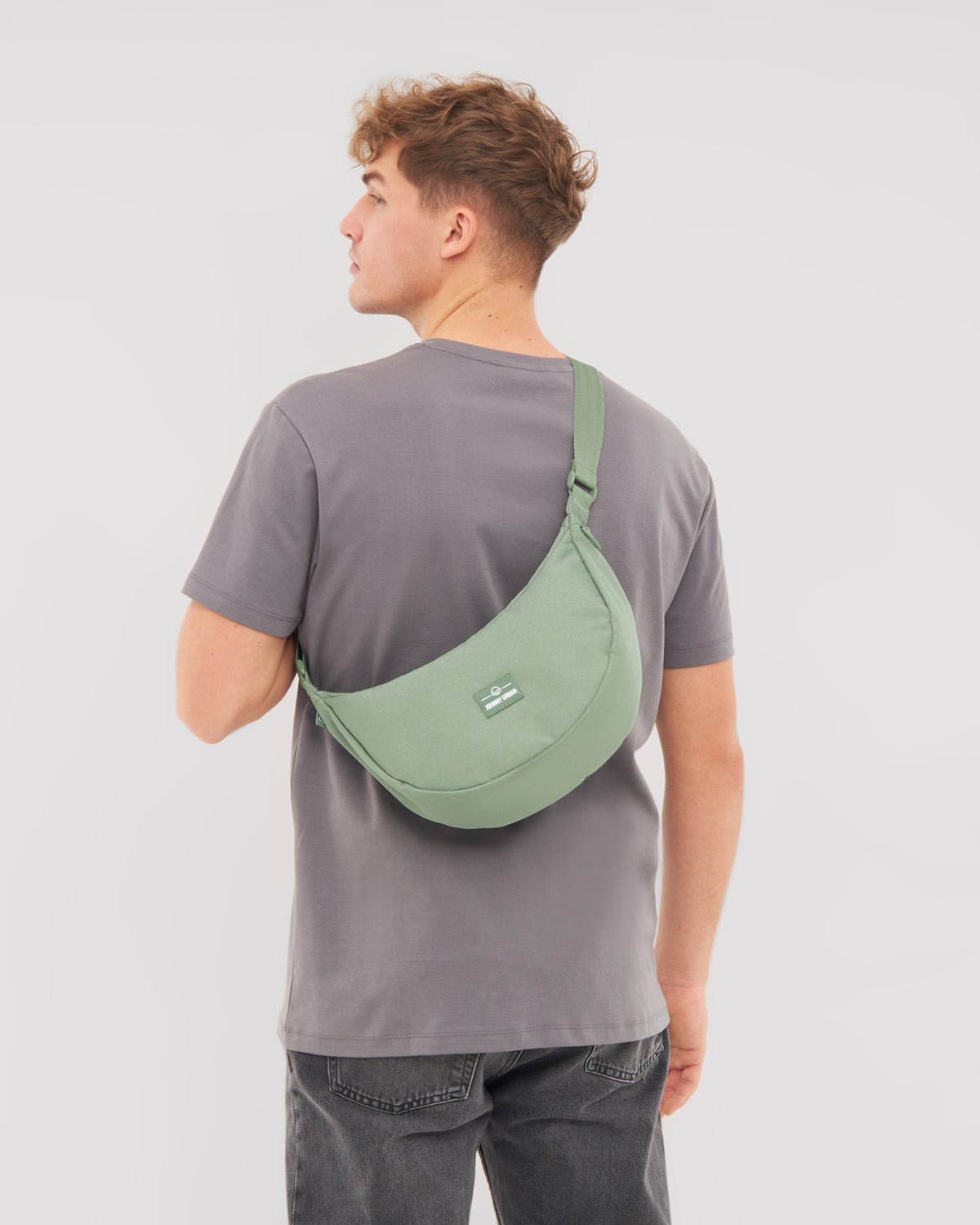 Mann von hinten trägt Half Moon Bag 'Ally Medium' in grün über grauem T-Shirt und dunkler Jeans