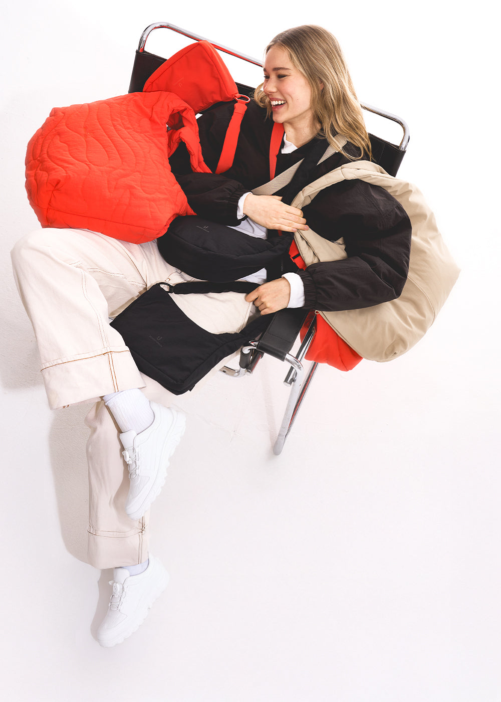 Frau sitzt mit einem Lachen im Sessel und hat alle Johnny Urban Taschen über sich gelegt.