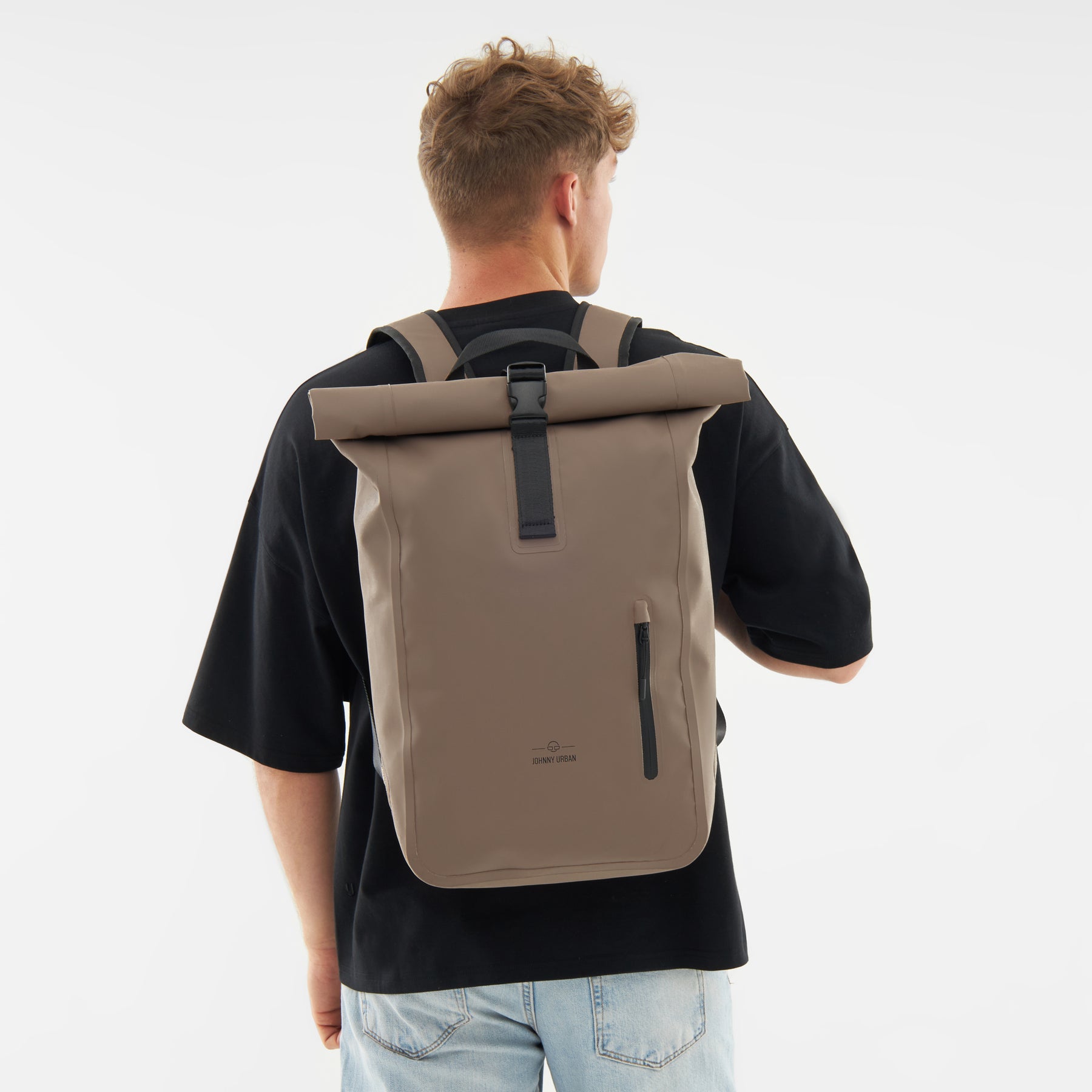 Mann von hinten mit beigem Rolltop Rucksack 'Conor' von Johnny Urban, schwarzes T-Shirt, blaue Jeans