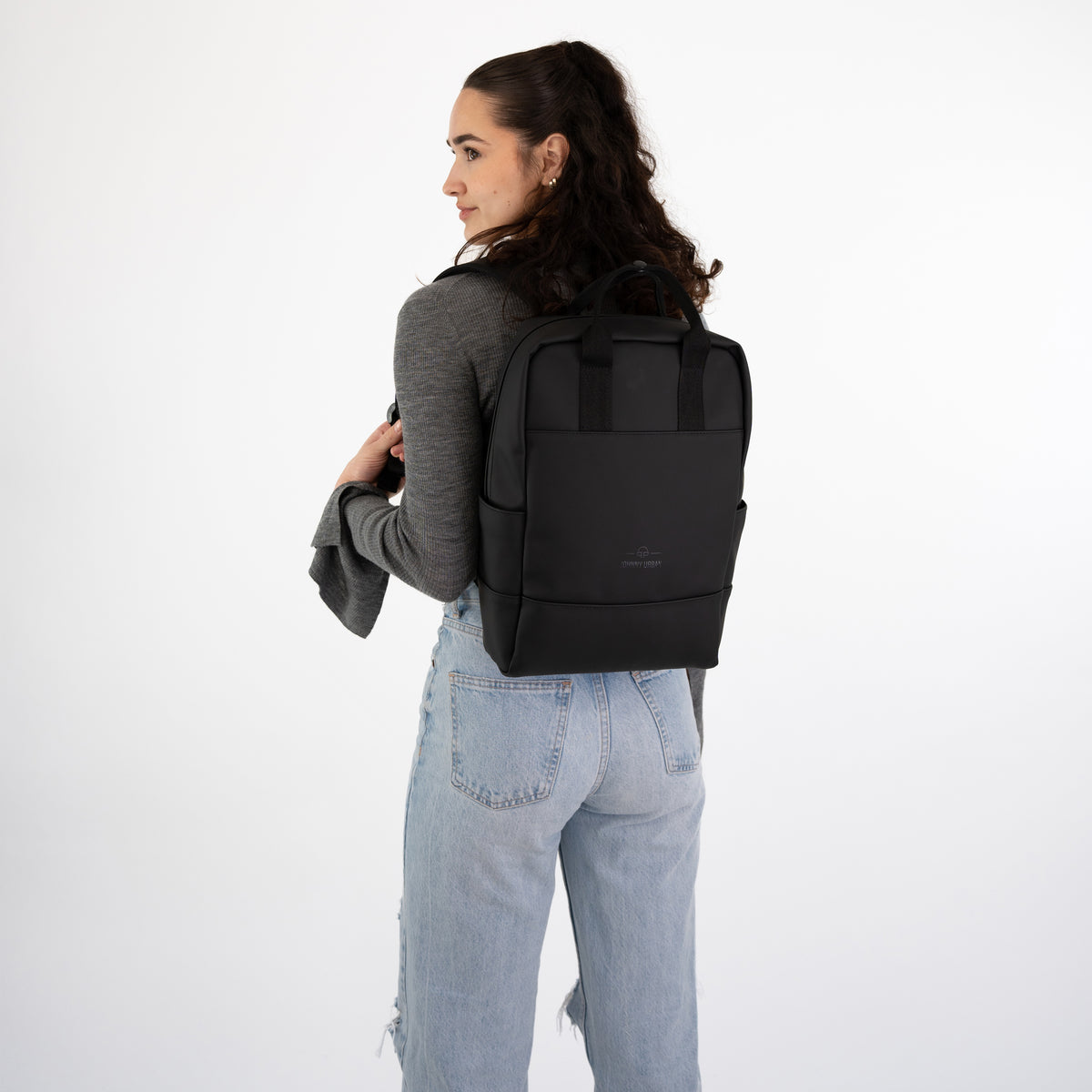 Frau mit schwarzen Rucksack 'Hailey' trägt grauen Pullover und hellblaue Jeans