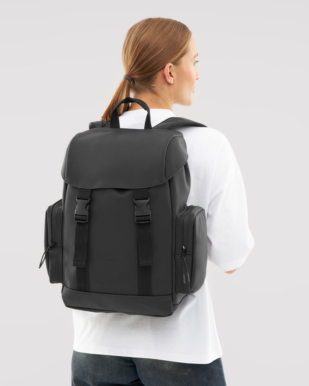 Schwarzer Rucksack 'Finley' mit seitlichen Reißverschlusstaschen, getragen von Frau mit weißem Shirt und Zopf