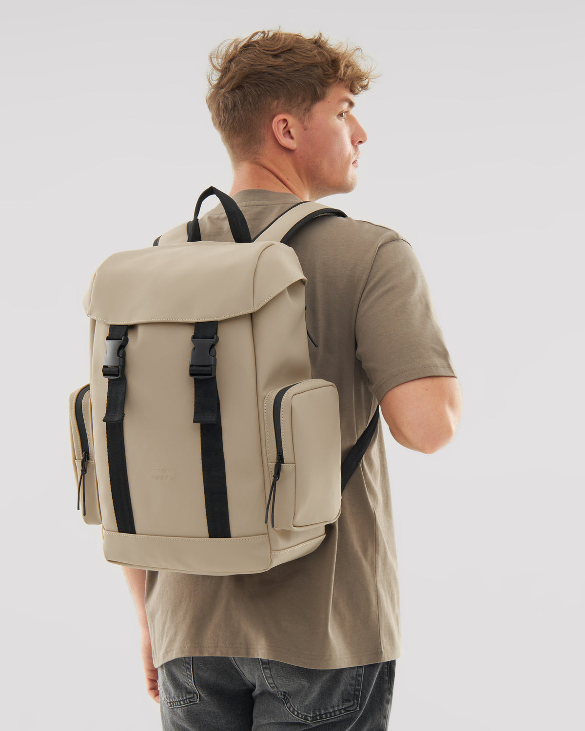 Mann trägt beigen Rucksack 'Finley' mit schwarzen Verschlüssen und seitlichen Taschen