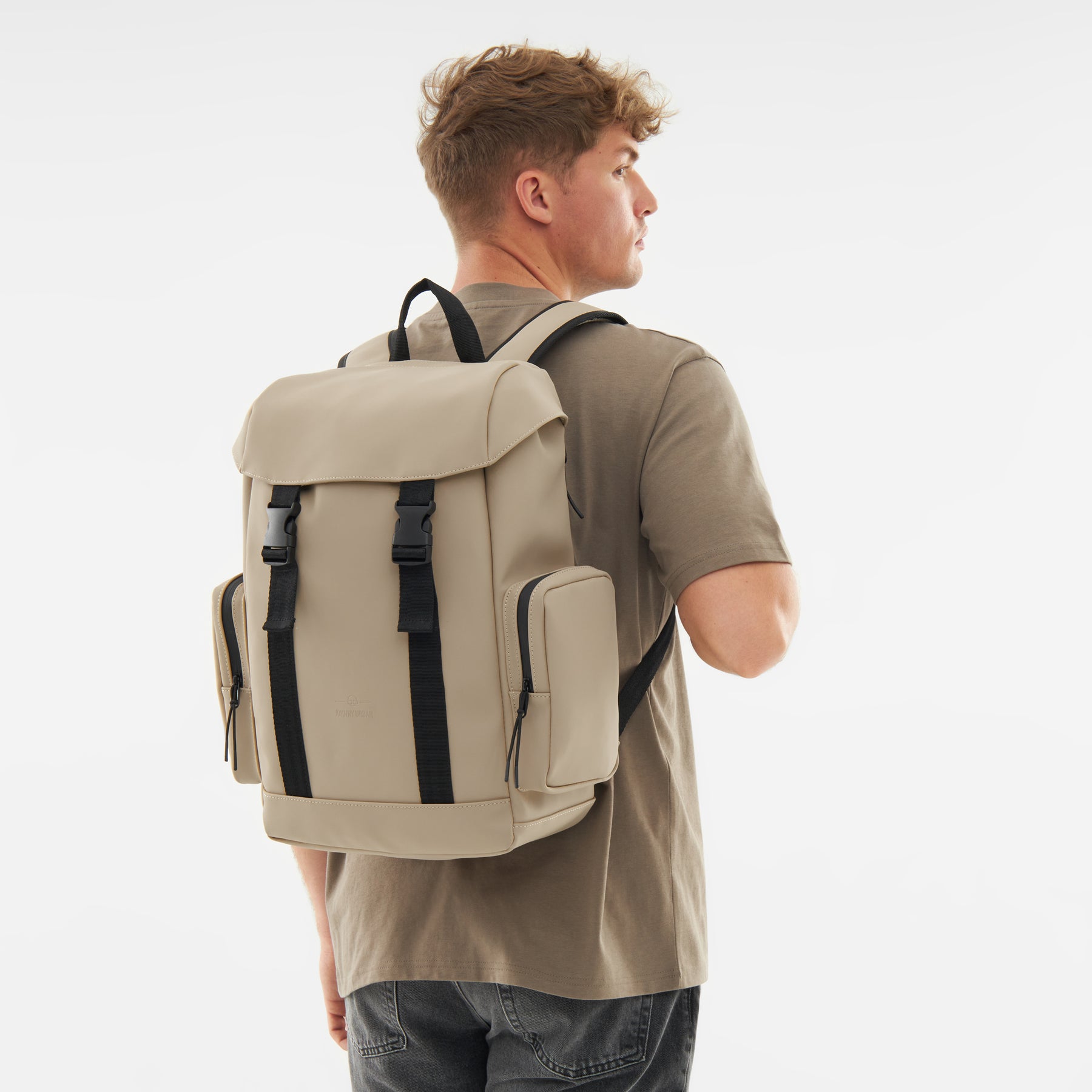 Mann trägt beigen Rucksack 'Finley' mit schwarzen Verschlüssen und seitlichen Taschen