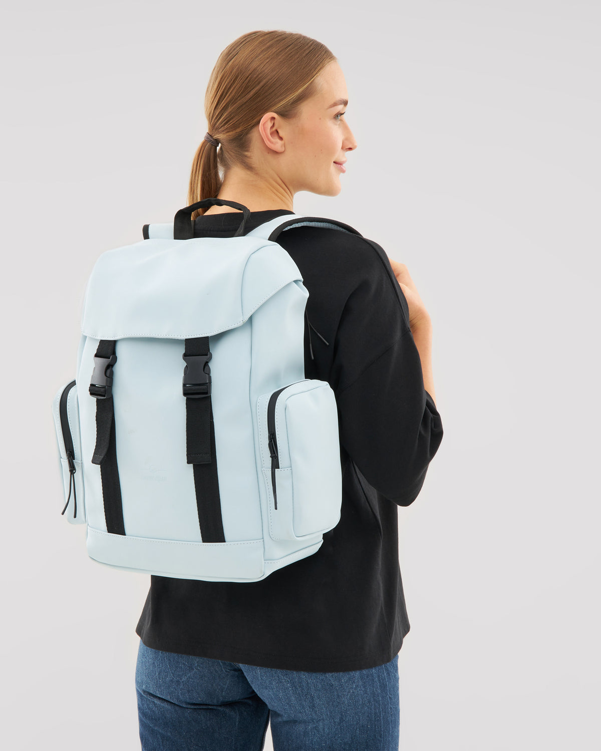 Frau mit hellblauem 'Finley' Rucksack von Johnny Urban, schwarzes Oberteil, blaue Jeans