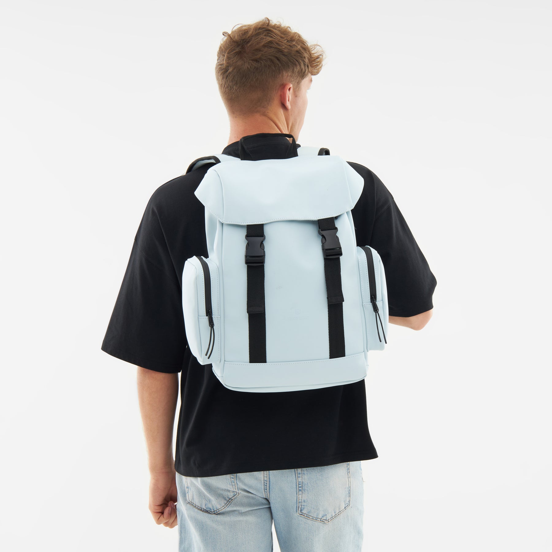 Hellblauer Rucksack 'Finley' mit zwei seitlichen Reißverschlusstaschen, getragen von einem Mann in schwarzem T-Shirt und hellen Jeans
