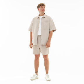 Männliches Modell trägt Sandfarbene Shorts und Kurzarm-Hemd aus dem Set 'Mason' mit weißen Turnschuhen
