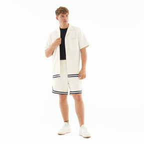 Mann trägt cremefarbene Shorts 'Parker' mit schwarzem Saum kombiniert mit cremefarbener Kurzarmjacke und weißen Sneakern