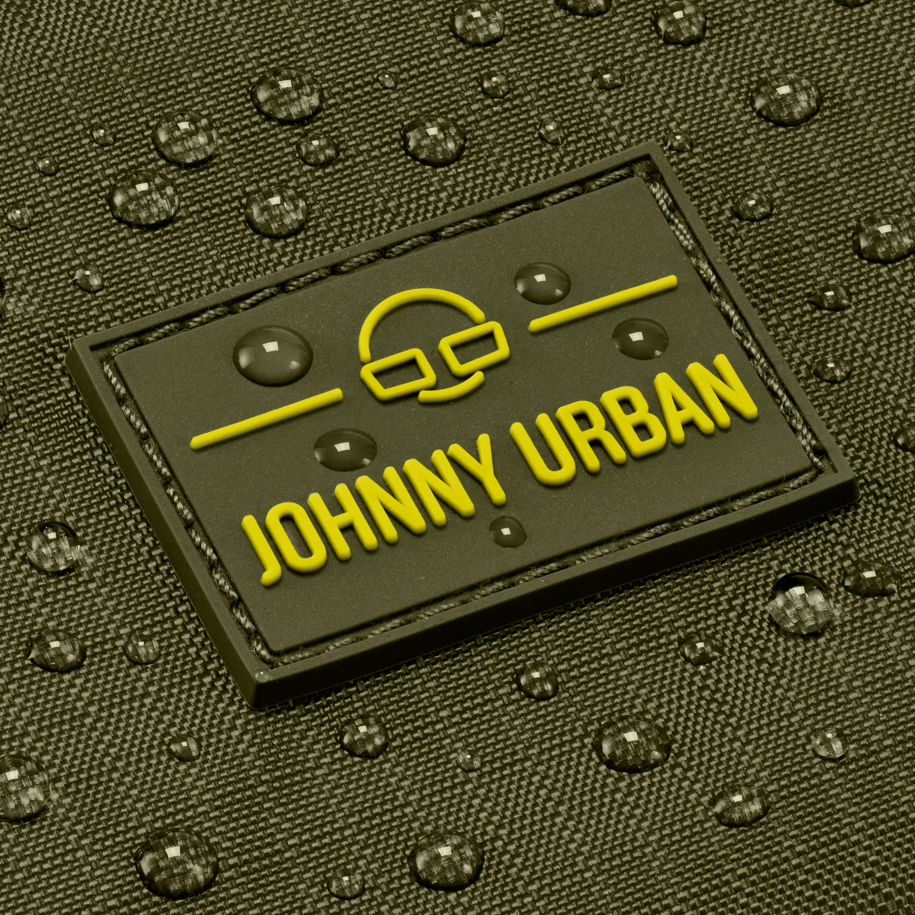 Nahaufnahme der wasserabweisenden Oberfläche und des gelben Johnny Urban Logos auf olivgrüner Umhängetasche 'Jayden'