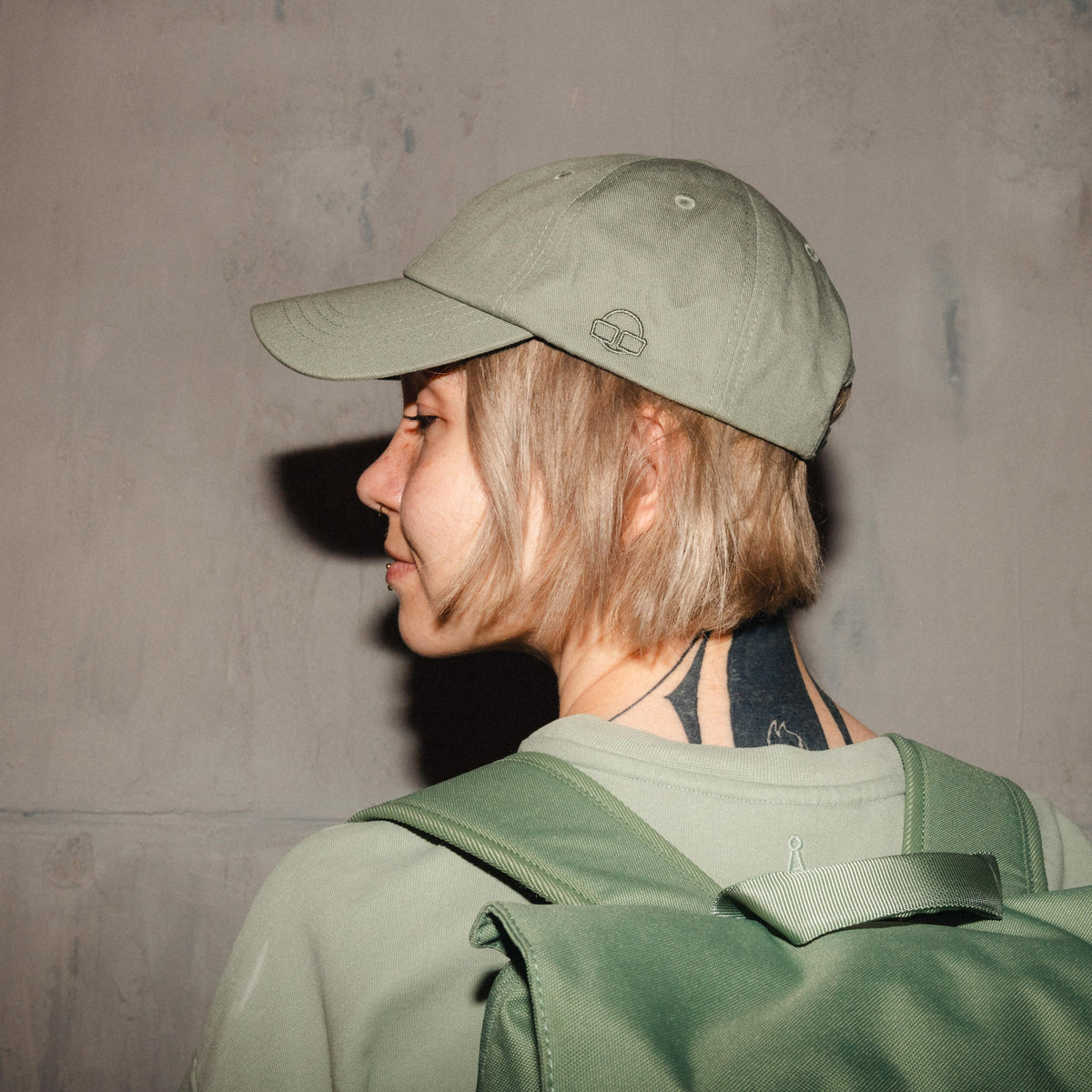 Grüne Canvas-Basecap 'Jen' von Johnny Urban auf kurzhaariger Frau mit grünem Rucksack