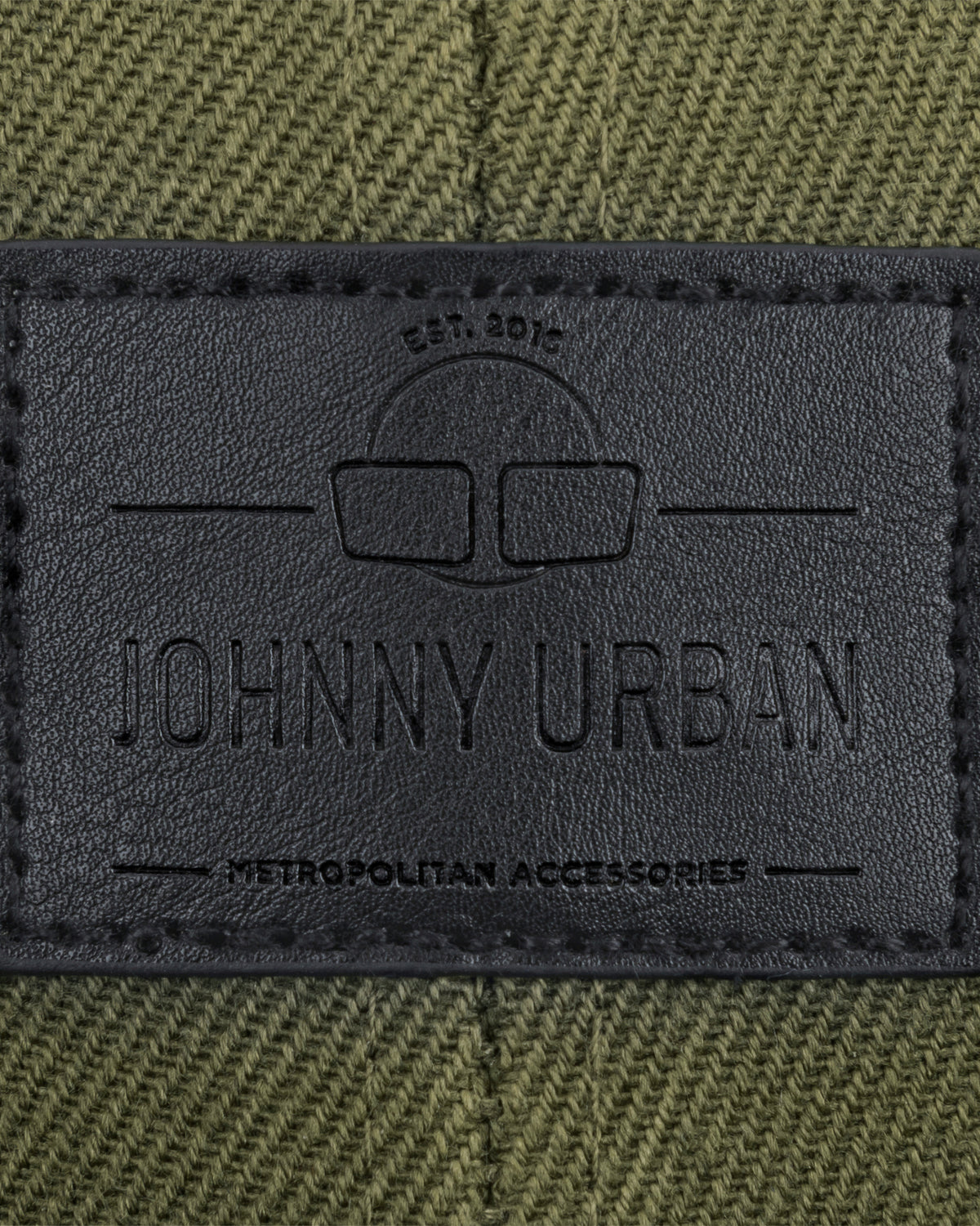 Schwarzes Lederlabel mit eingeprägtem Johnny Urban Logo und Text auf grünem Stoff
