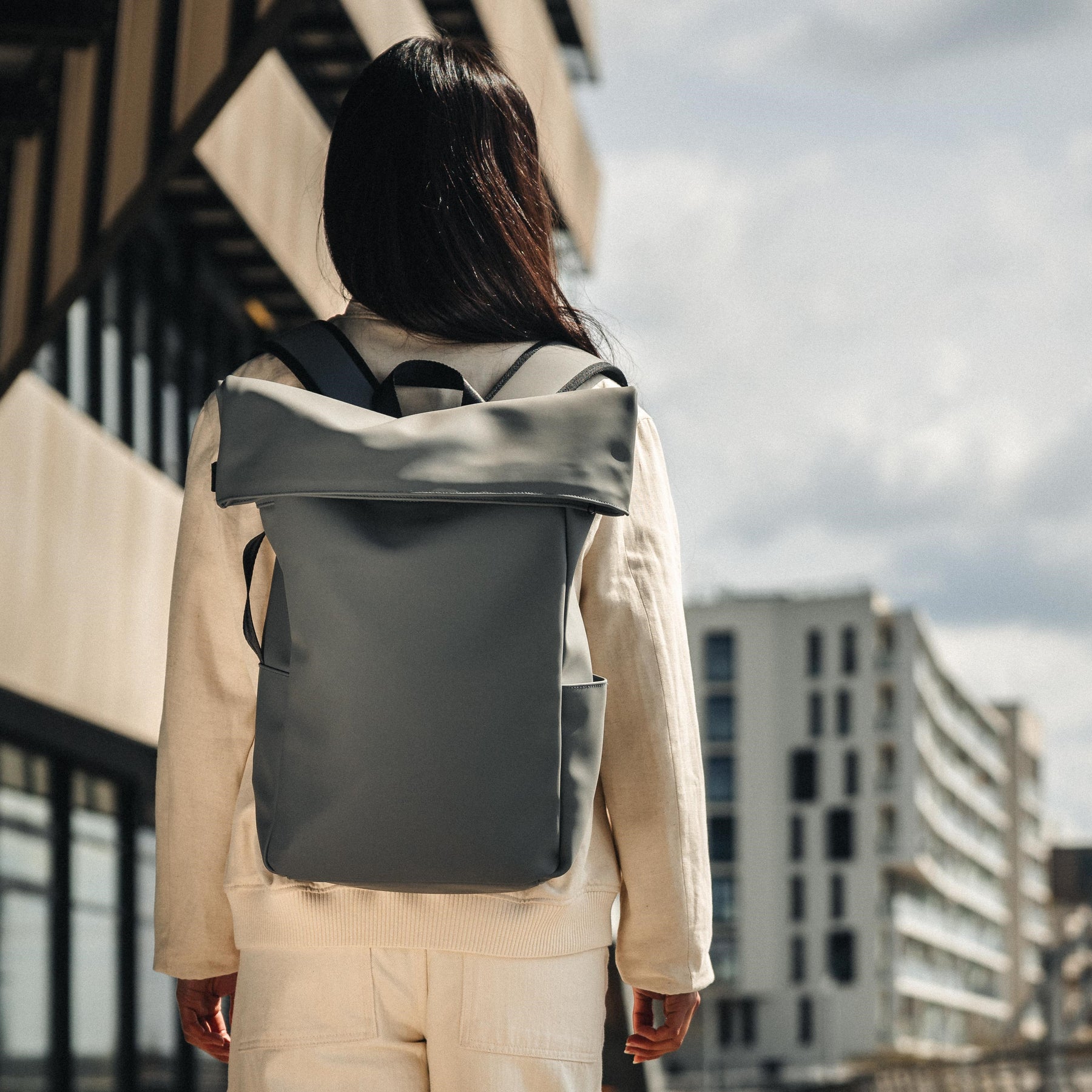 Dame von hinten mit hellem Outfit trägt grauen Rolltop-Rucksack 'Henry' von Johnny Urban in urbaner Umgebung