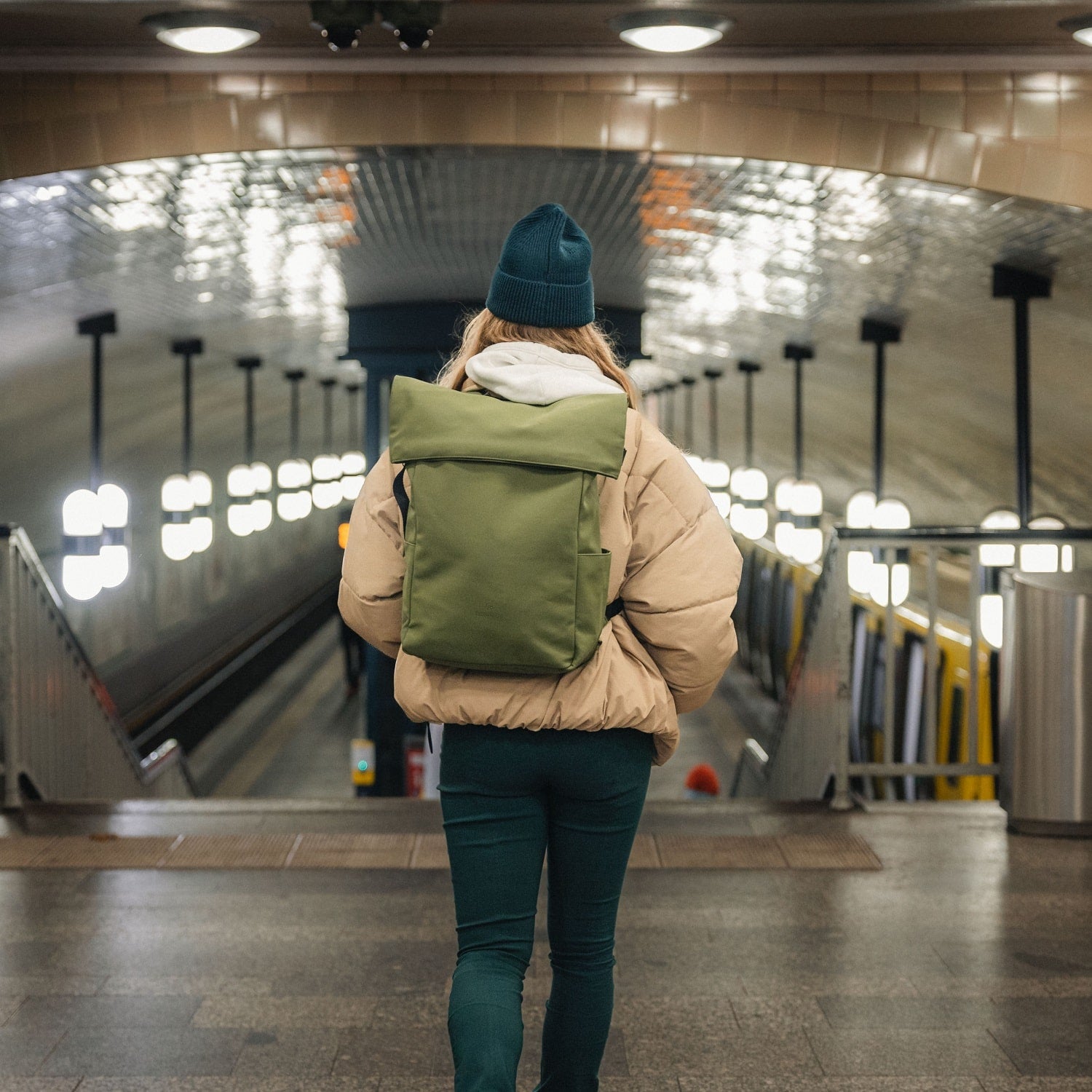 Frau trägt den olivgrünen Rolltop Rucksack 'Henry' in einer U-Bahn-Station