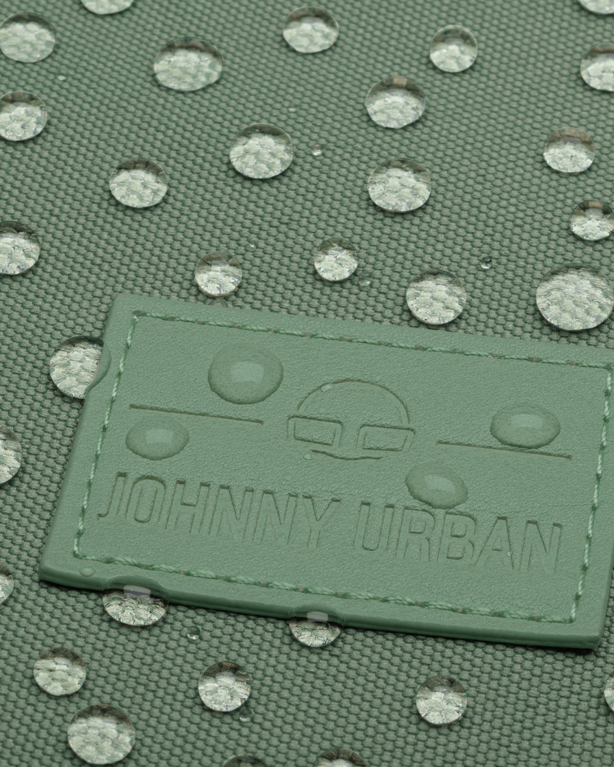 Grünes wasserdichtes Gewebe mit wasserabweisenden Tropfen und Johnny Urban Logo auf einem Rolltop Rucksack