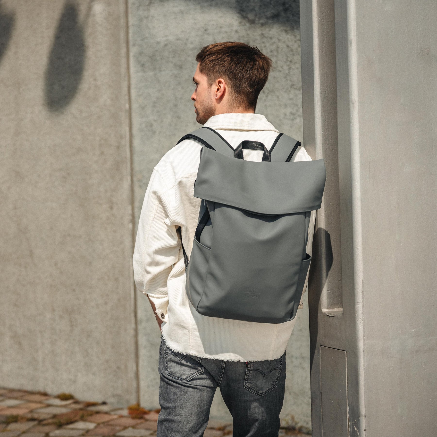 Mann trägt grauen Rolltop Rucksack 'Henry' von Johnny Urban mit weißem Hemd und grauer Jeans