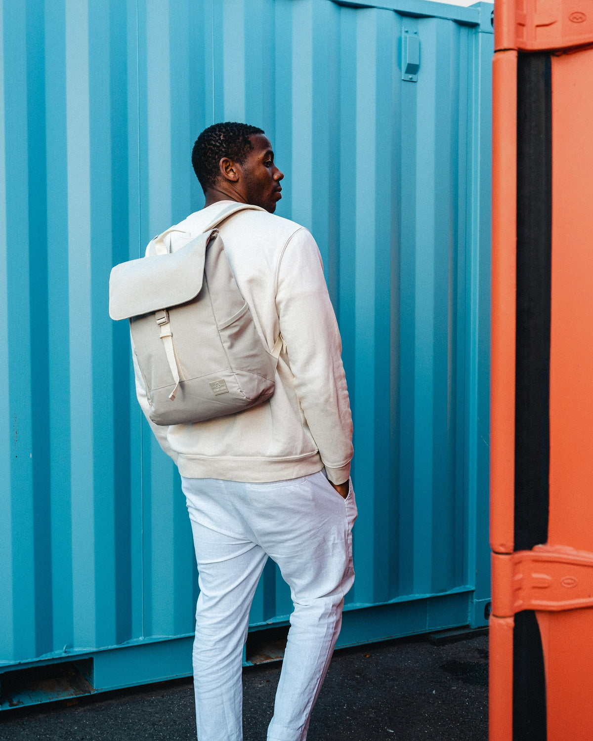 Mann trägt beigen Johnny Urban Rucksack 'Mika' vor blauem Container