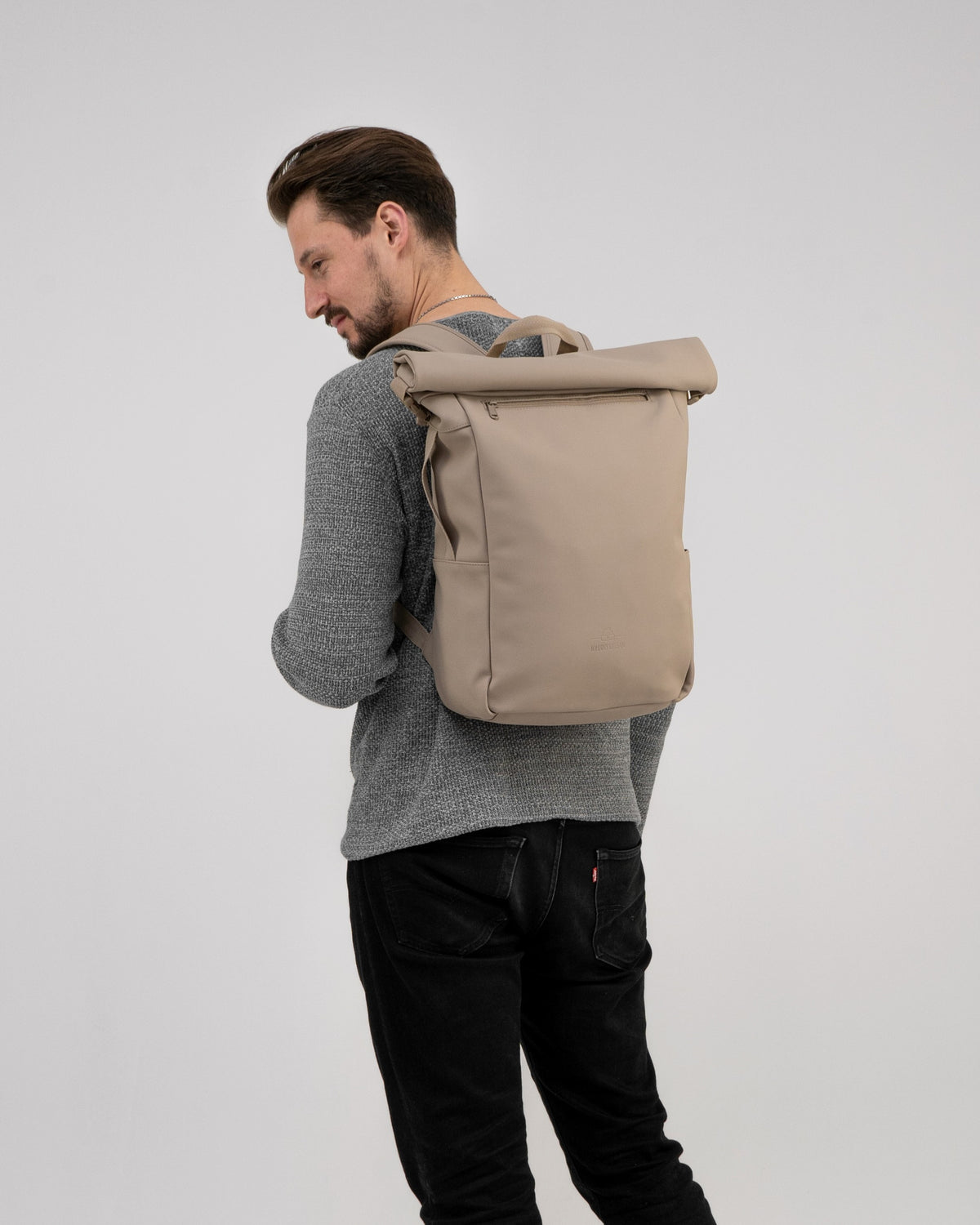 Mann trägt beigen Rolltop Rucksack 'Henry' von Johnny Urban mit grauem Pullover und schwarzer Hose