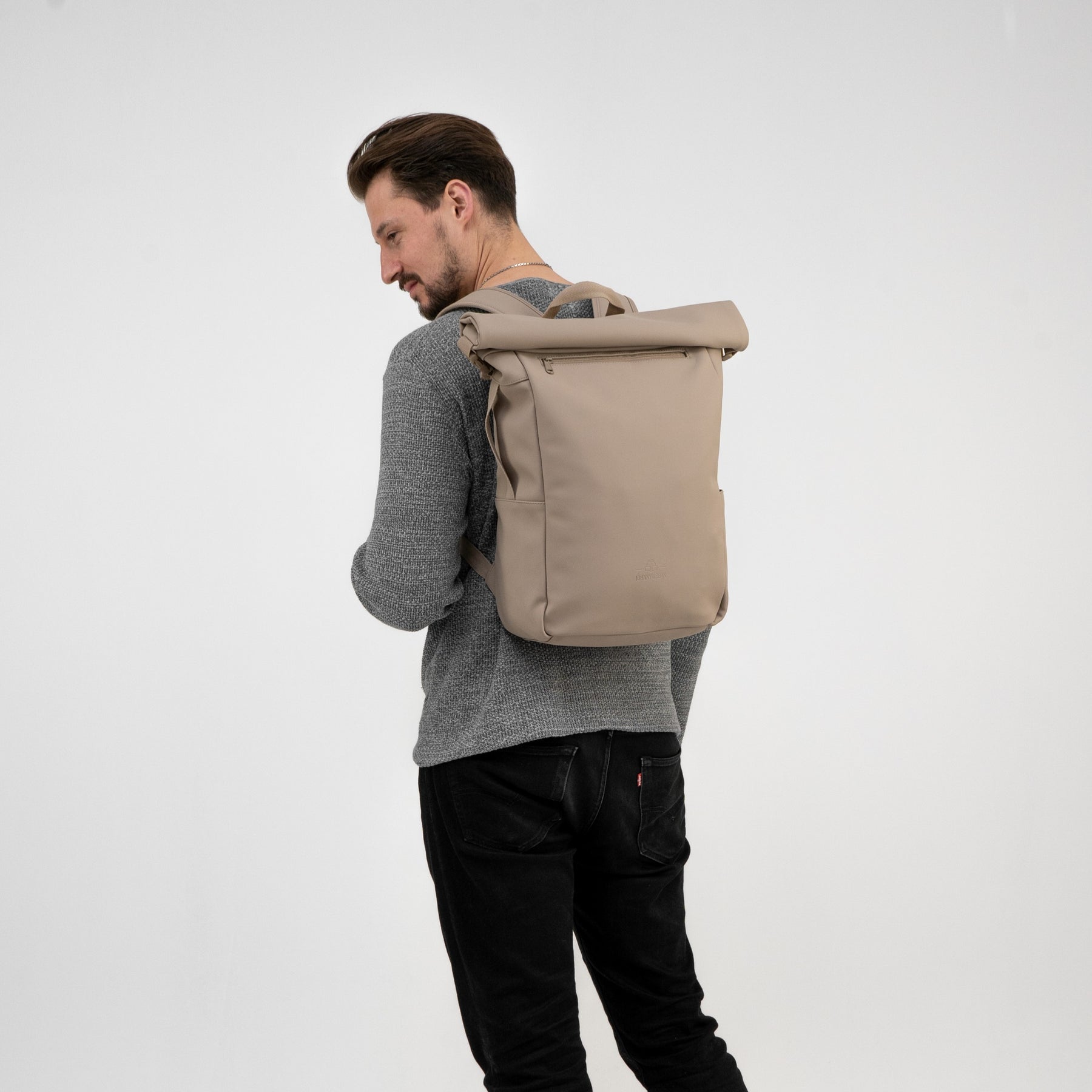Mann trägt beigen Rolltop Rucksack 'Henry' von Johnny Urban mit grauem Pullover und schwarzer Hose